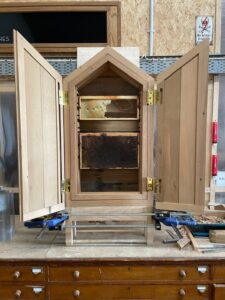 A wooden beehive cabinet with open doors, showing two honeycombs stored on internal racks.