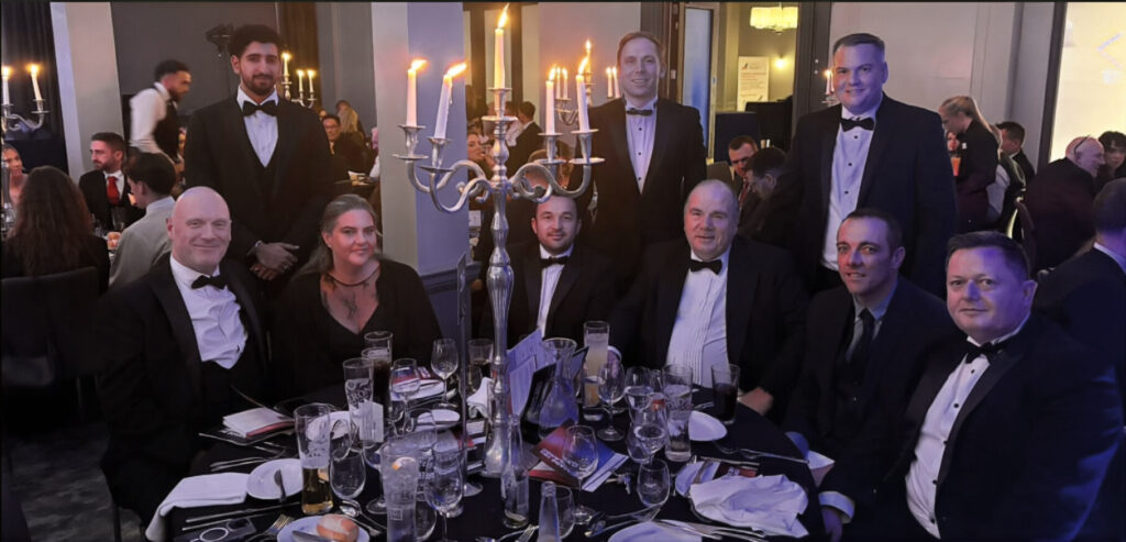 A group of people in formal wear at a dinner table with a candelabra centrepiece.